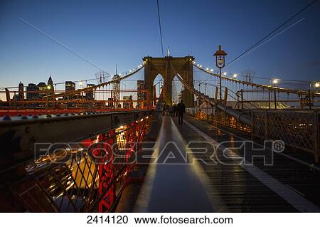 Stock Image - Pedestrian path on Brooklyn Bridge heading into Manhattan at night; New York City, New York, United States of America. Fotosearch