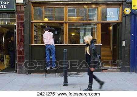Stock Photograph - Pedestrian walking beside retail shops, Brick Lane; London, England. Fotosearch
