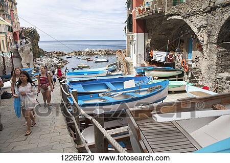 Stock Image - Pedestrians and boats lining the walkway; Riomaggiore, Liguria, Italy. Fotosearch
