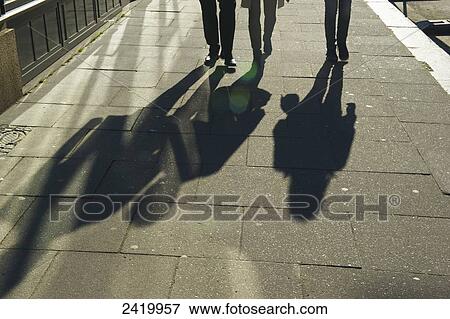 Stock Photo - Pedestrians and their shadows cast on the sidewalk at sunrise; Hamburg, Germany. Fotosearch