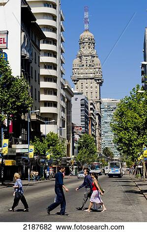 Stock Image - Pedestrians Crossing 18Th Of July Avenue And Views Of Salvo Palace, Historical Building Built In 1922-28, Eclecticism Style, Montevideo, Uruguay, South America. Fotosearch