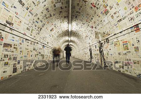 Stock Image - Pedestrians In A Tunnel With Walls Covered In Newspaper; Lugano, Ticino, Switzerland. Fotosearch