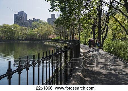 Stock Photograph - Pedestrians on a park path at the water's edge; New York City, New York, United States of America. Fotosearch