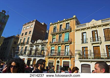 Stock Photo - Pedestrians walk on a street with residential buildings and blue sky; Barcelona, Spain. Fotosearch
