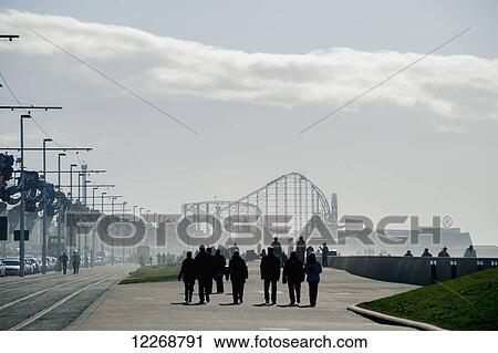 Pedestrians walking along the promenade in the mist with a roller coaster in the distance; Blackpool, Lancashire, England View Large Photo Image Stock Image - Pedestrians walking along the promenade in the mist with a roller coaster in the distance; Blackpool, Lancashire, England. Fotosearch
