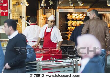 Stock Image - Pedestrians Walking By A Vendor Of At Shop Selling Roasting Poultry; Istanbul Turkey. Fotosearch