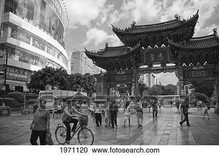 Stock Image - Pedestrians Walking In An Urban Area Beside New Era Hotel; Kunming Yunnan China. Fotosearch