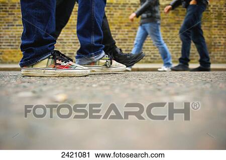 Stock Image - Pedestrians walking on a sidewalk of Portobello Road beside a brick building; London, England. Fotosearch