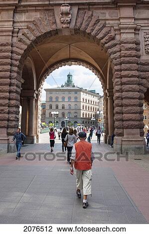 Stock Image - Pedestrians Walking Through An Arch At Parliament House; Stockholm Sweden. Fotosearch