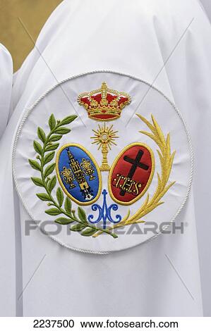 Stock Image - Penitente Displaying The Coat Of Arms Of The Brotherhood Of The Peace Of Sevilla Outside The Iglesia De San Sebastian; Seville Spain. Fotosearch