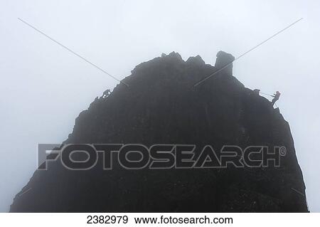Stock Photo - People climbing the Inaccessible Pinnacle on the left side while others abseil off the right side in misty conditions, Sgurr Dearg; Isle of Skye, Scotland. Fotosearch