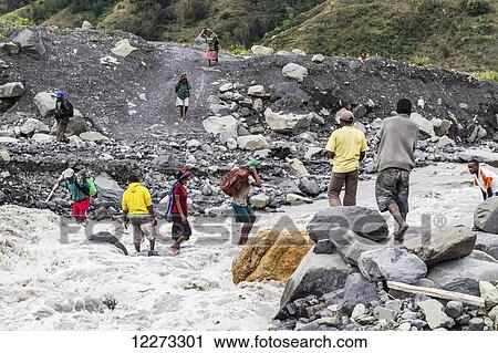 Stock Image - People crossing a torrentous stream after a bridge was washed out in the Baliem Valley, Central Highlands of Western New Guinea, Papua, Indonesia. Fotosearch