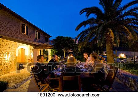 Stock Image - People Dining At Outdoor Table At Dusk. Fotosearch
