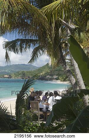 Stock Photograph - People Having Their Lunch Beneath Palm Trees At The Aquarium Restaurant, Point Salines Beach, Grenada.. Fotosearch