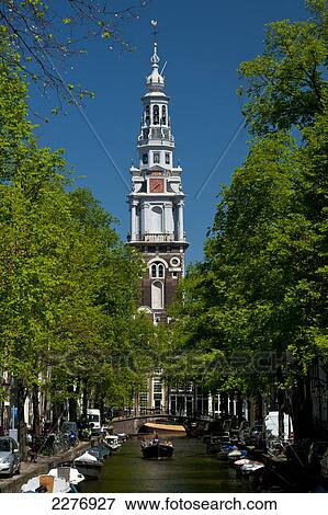 Stock Photo - People in small boat going along small canal with spire of the Zuiderkerk church behind; Amsterdam, Holland. Fotosearch