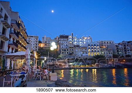 Stock Photo - People In Waterfront Cafes At Xlendi Bay At Dusk. Fotosearch