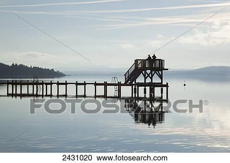 Stock Image - People on an elevated lookout at the end of a pier on a lake with fog; Herrsching, Bavaria, Germany. Fotosearch