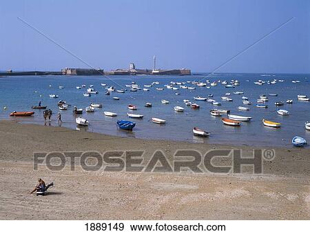 Stock Photo - People On Beach With Boats Moored In Ocean, Elevated View. Fotosearch