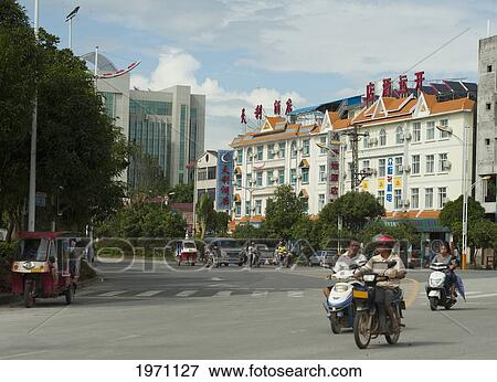 Stock Photo - People Riding Motorized Scooters Down The Street; Mangshi Yunnan China. Fotosearch