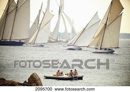Stock Image - People Sit On A Floating Dock And Watch The Sailboats Off The Coast; Cannes Provence France. Fotosearch