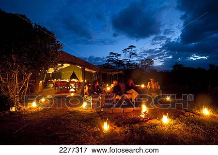 Stock Photo - People sitting around fire at dusk in front of dining tent, Ol Pejeta Camp, Ol Pejeta Conservancy; Kenya. Fotosearch