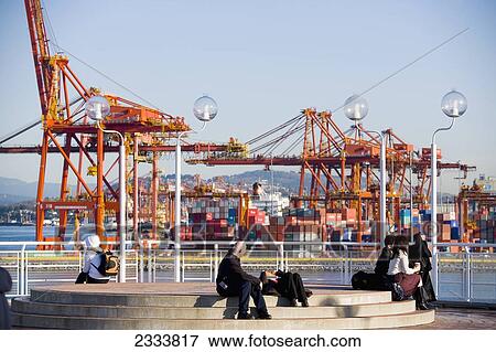Stock Photo - People Sitting With Crane In Background, Vancouver Waterfront, Harbor; Vancouver, British Columbia, Canada. Fotosearch