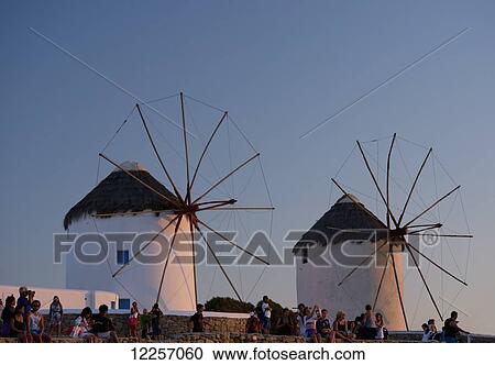 Stock Image - People watching the sunset beneath old windmills; Mykonos Town, Mykonos, Cyclades, Greek Islands, Greece. Fotosearch