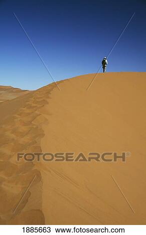 Stock Image - Person Climbing Sand Dunes In Namib Desert. Fotosearch