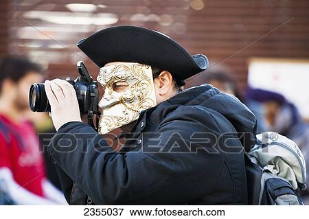 Stock Photo - Person in Venetian costume during Venice carnival taking a photograph; Venice, Italy. Fotosearch