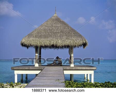 Stock Image - Person Receiving Massage On Pier With Grass Hut. Fotosearch
