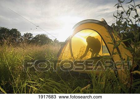Stock Image - Person Setting Up Tent In Meadow. Fotosearch
