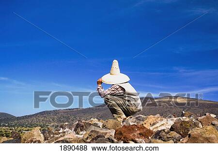 Stock Photo - Person Sitting On Rocks Overlooking Landscape. Fotosearch