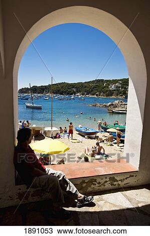 Stock Image - Person Sitting Under Arch Near Beach In Calella Fishing Village. Fotosearch