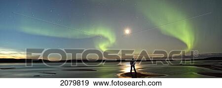 Stock Photo - Person Standing Under The Aurora Borealis While The Mackenzie River Flows By, Fort Simpson, Nwt.. Fotosearch