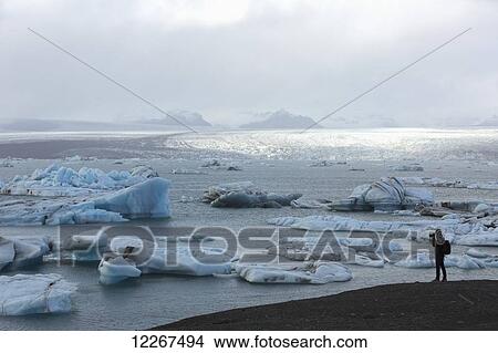 Picture - Photographer taking photos of icebergs at a glacial lagoon called Jokulsarlon on the south coast of Iceland; Iceland. Fotosearch
