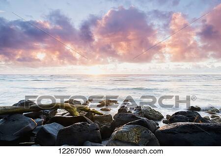 Stock Image - Pink glowing clouds at sunrise; Wailua, Kauai, Hawaii, United States of America. Fotosearch