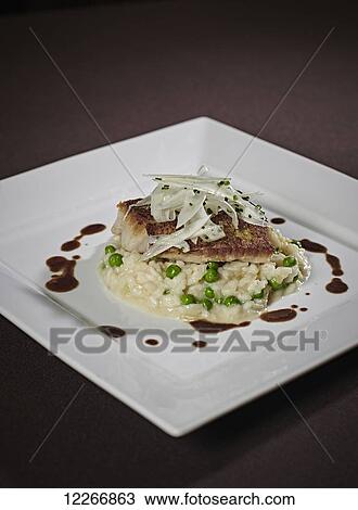 Stock Image - Plated dinner of artichoke topped fish steak with risotto and peas drizzled with balsamic vinegar; Ontario, Canada. Fotosearch