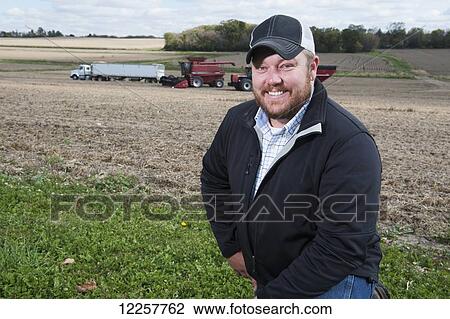Stock Image - Portrait of a farmer with his farmland and equipment in the background; Minnesota, United States of America. Fotosearch