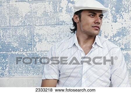 Stock Photo - Portrait of a man with with a white hat, leaning against blue wall; Honolulu, Oahu, Hawaii, United States of America. Fotosearch