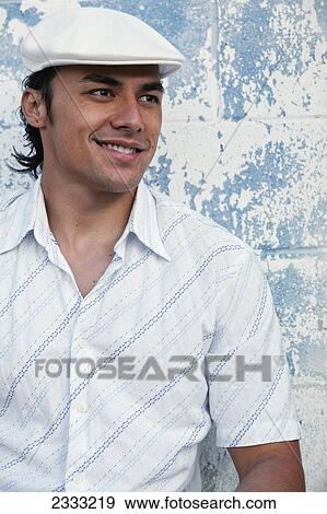 Stock Photo - Portrait of a man with with a white hat, leaning against blue wall; Honolulu, Oahu, Hawaii, United States of America. Fotosearch
