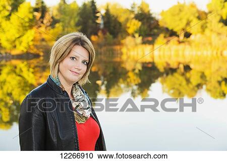 Stock Image - Portrait of a mature woman in a park beside a lake in autumn; Edmonton, Alberta, Canada. Fotosearch