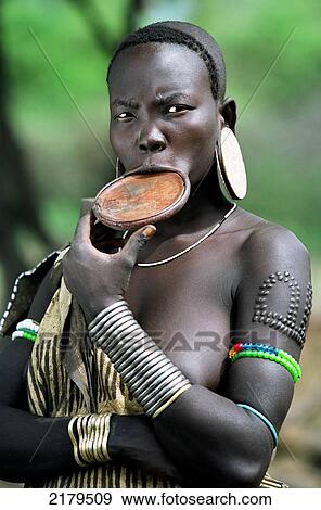 Stock Photo - Portrait of a Mursi tribal woman displaying pierced ear lobes & lower lip (to hold a traditional 'debhi a tugoin' - lip plate) and scar tattoos. Makki / South Omo / Southern Nations, Nationalities & People's Region (Ethiopia).. Fotosearch