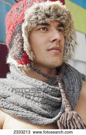 Stock Image - Portrait of a shirtless young man wearing a scarf and fur trimmed hat standing against a colourful wall; Honolulu, Oahu, Hawaii, United States of America. Fotosearch