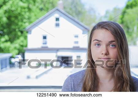Stock Image - Portrait of a teenage girl in front of a house; Connecticut, United States of America. Fotosearch
