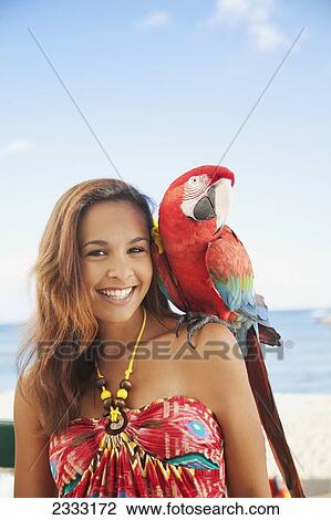 Stock Image - Portrait of a woman holding a colourful bird on her shoulder; Waikiki, Oahu, Hawaii, United States of America. Fotosearch