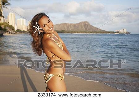Portrait of a woman on a beach in a bikini at sunset with a tropical flower in her hair; Waikiki, Oahu, Hawaii, United States of America View Large Photo Image Picture - Portrait of a woman on a beach in a bikini at sunset with a tropical flower in her hair; Waikiki, Oahu, Hawaii, United States of America. Fotosearch