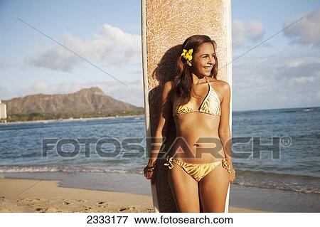 Stock Photo - Portrait of a woman on a beach in a bikini holding a surfboard; Waikiki, Oahu, Hawaii, United States of America. Fotosearch