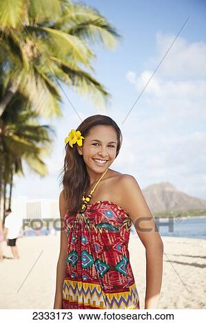 Stock Image - Portrait of a woman on a beach with a tropical flower in her hair; Waikiki, Oahu, Hawaii, United States of America. Fotosearch