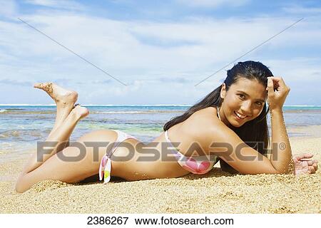 Portrait of a young woman in a bikini laying on the sand; Hawaii, United States of America View Large Photo Image Stock Photo - Portrait of a young woman in a bikini laying on the sand; Hawaii, United States of America. Fotosearch