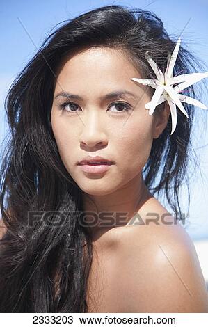 Stock Image - Portrait of a young woman with a white tiger lily in her dark hair; Oahu, Hawaii, United States of America. Fotosearch